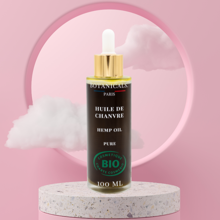 Une bouteille de 100ml d'huile de chanvre bio devant un fond rose, parsemé de léger nuage