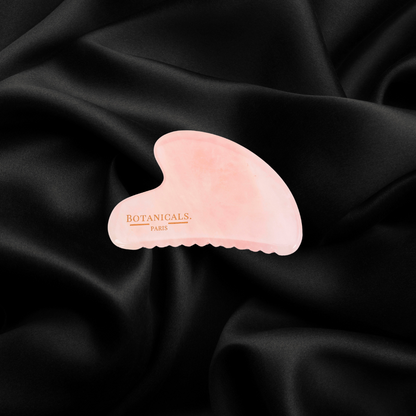 Guasha à dents Botanicals en Quartz rose devant un fond en soie de murier noir