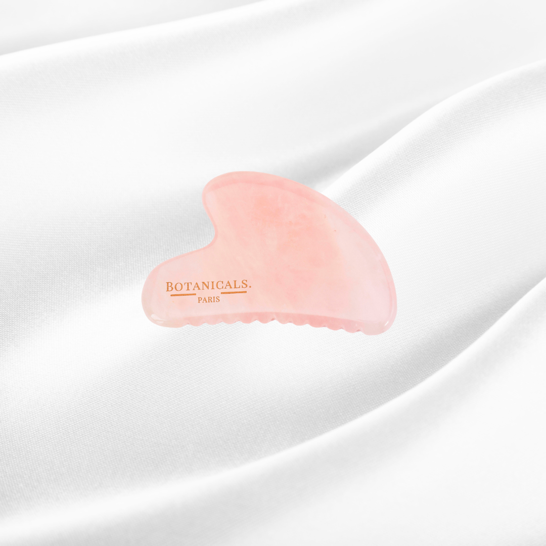 Guasha à dents Botanicals en Quartz rose devant un fond en soie de murier blanc
