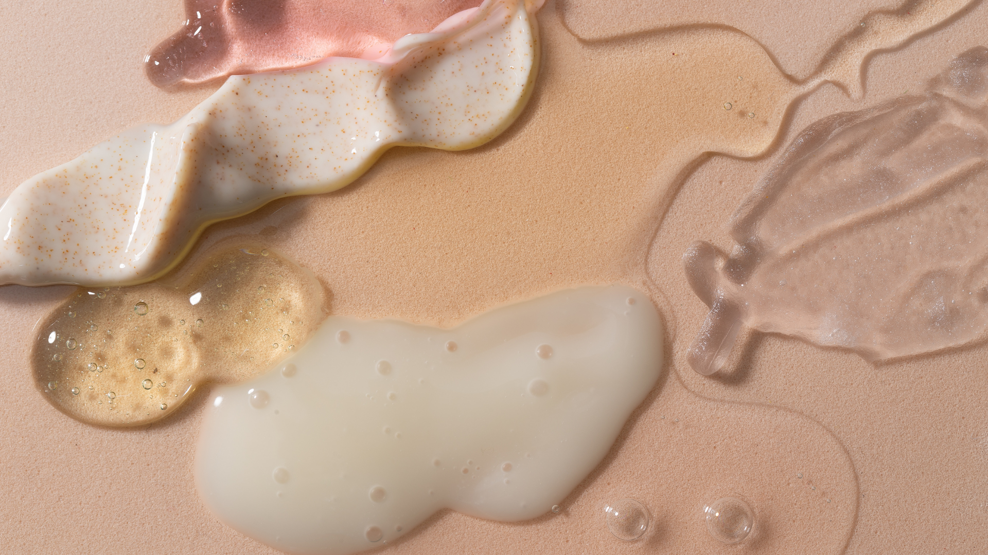 Un mélange d'huiles et de crèmes faisant apparaitre 6 différentes textures d'huiles et de cremes sur un fond beige poudreux