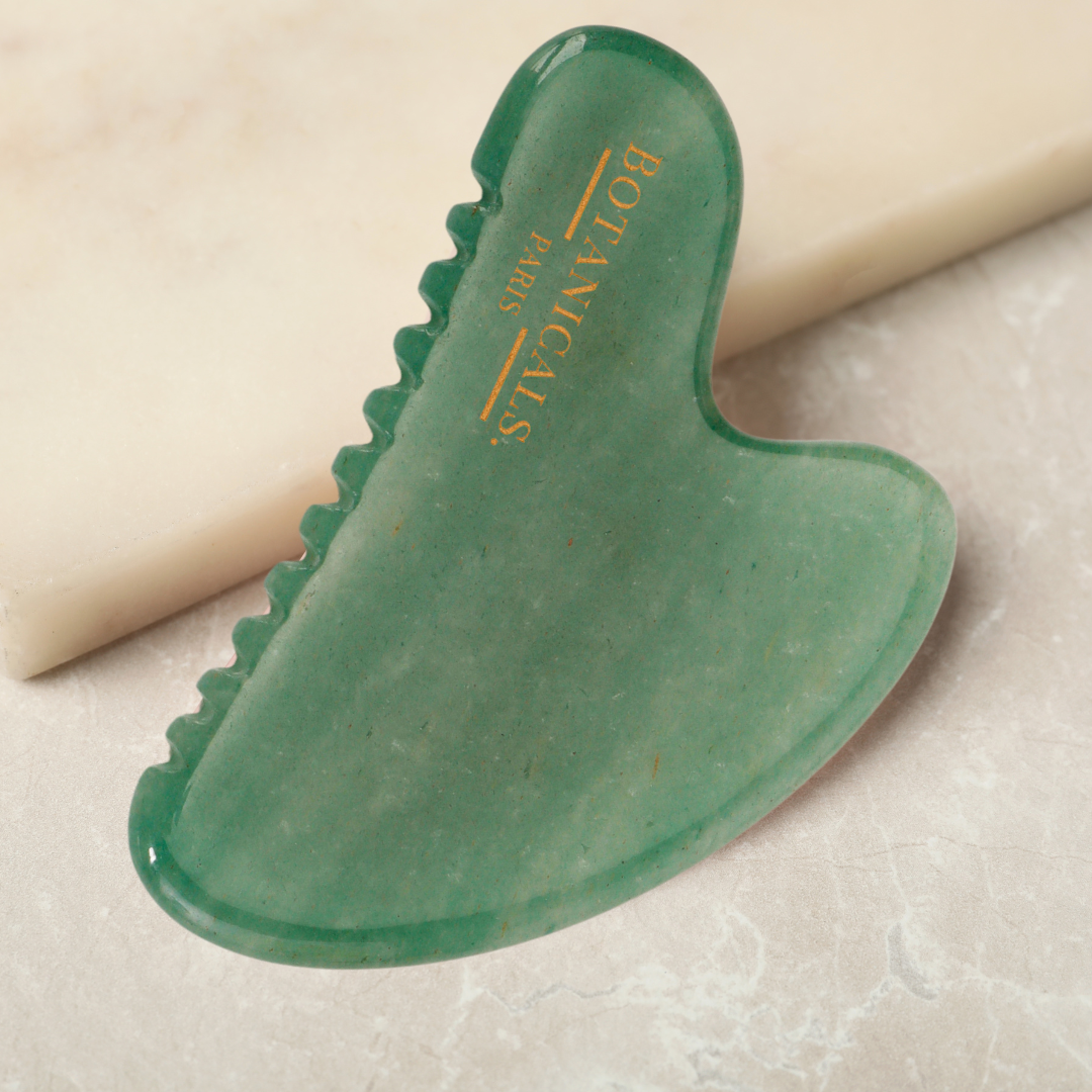 Un guasha à dents en Jade posé sur un marbre beige