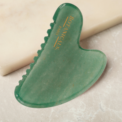Un guasha à dents en Jade posé sur un marbre beige