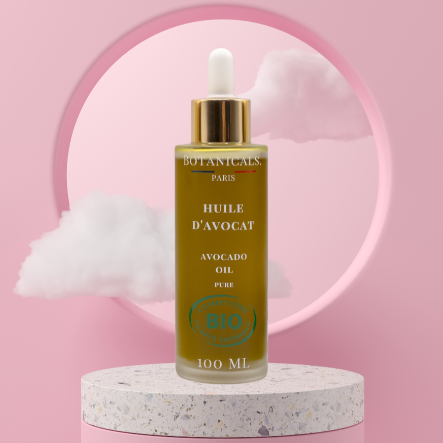 Une bouteille de 100ml d'huile d'avocat bio devant un fond rose, parsemé de léger nuage