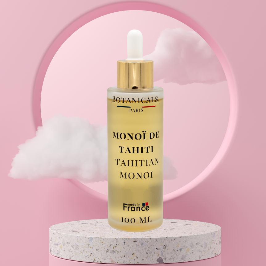 Une bouteille de 100ml de Monoi de Tahiti enrichi à l'huile de coco devant un fond rose, parsemé de léger nuage